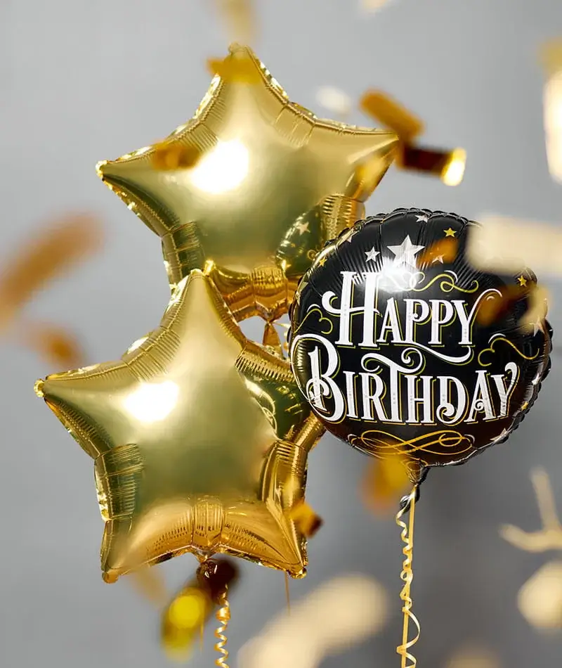 Three gold star balloons and a black balloon reading Happy Birthday float against a light background with falling gold confetti. Three gold star balloons and a black balloon reading Happy Birthday float against a light background with falling gold confetti.